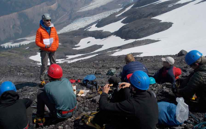 an instructor gives direction to a group of mountaineering students in a a rocky and snowy field